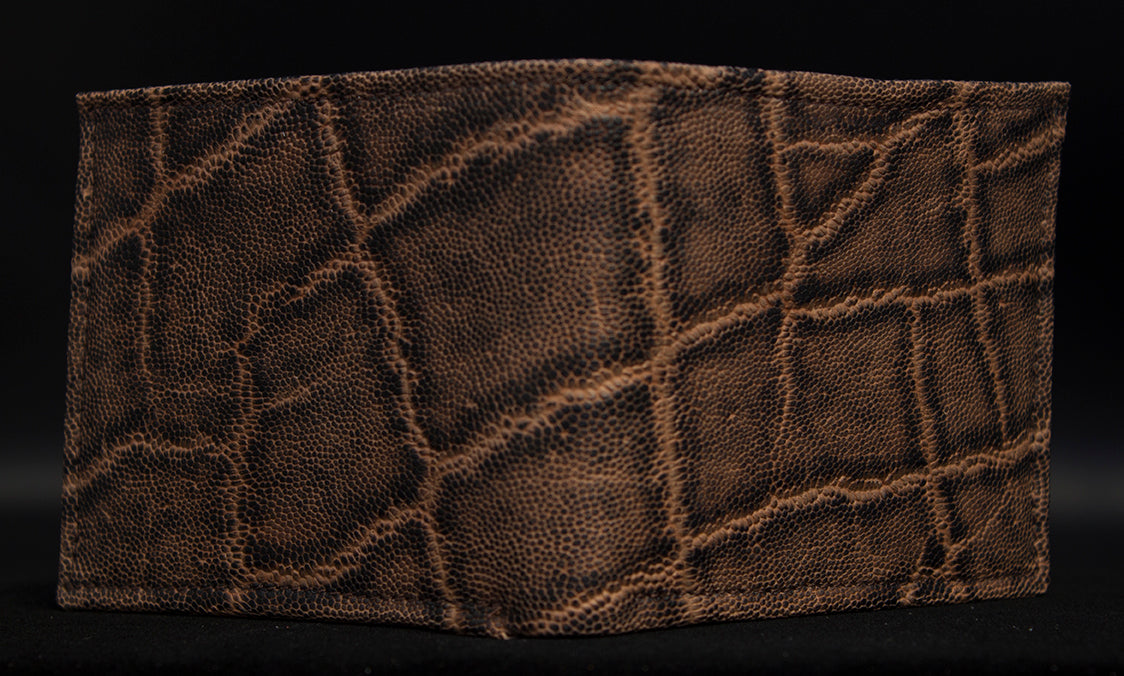 A traditional bi-fold wallet made from brown elephant leather, displayed in a folded state against a dark background.